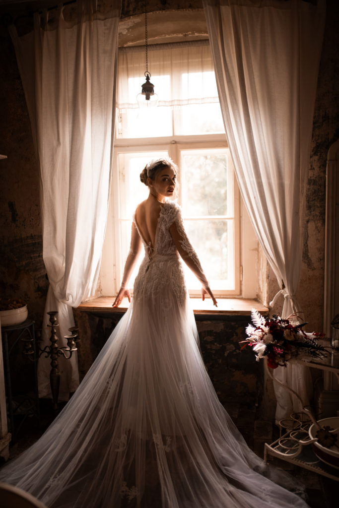 Die Braut steht vor einem Fenster mit Vorhang