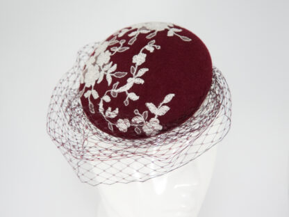 Fascinator in Buttonform aus bordeauxfarbigem Filz mit weißer Blütenspitze und bordeauxfarbigem Schleiertüll